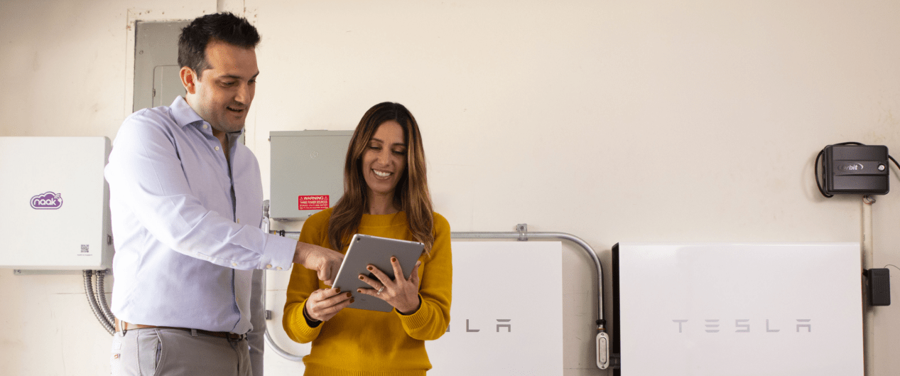 two people looking at a tablet in front of Tesla batteries